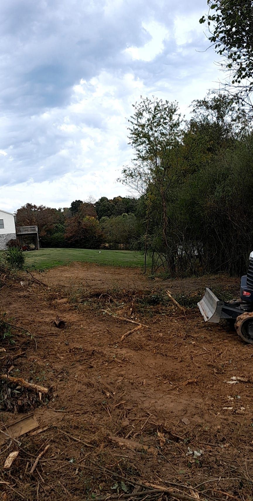 Dirt clearing with a small tractor; trees and cloudy sky in background.