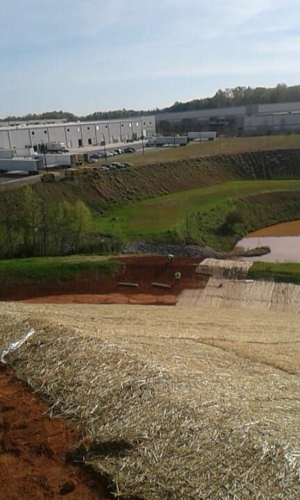 A grassy hillside with construction, leading to a commercial building with trucks.