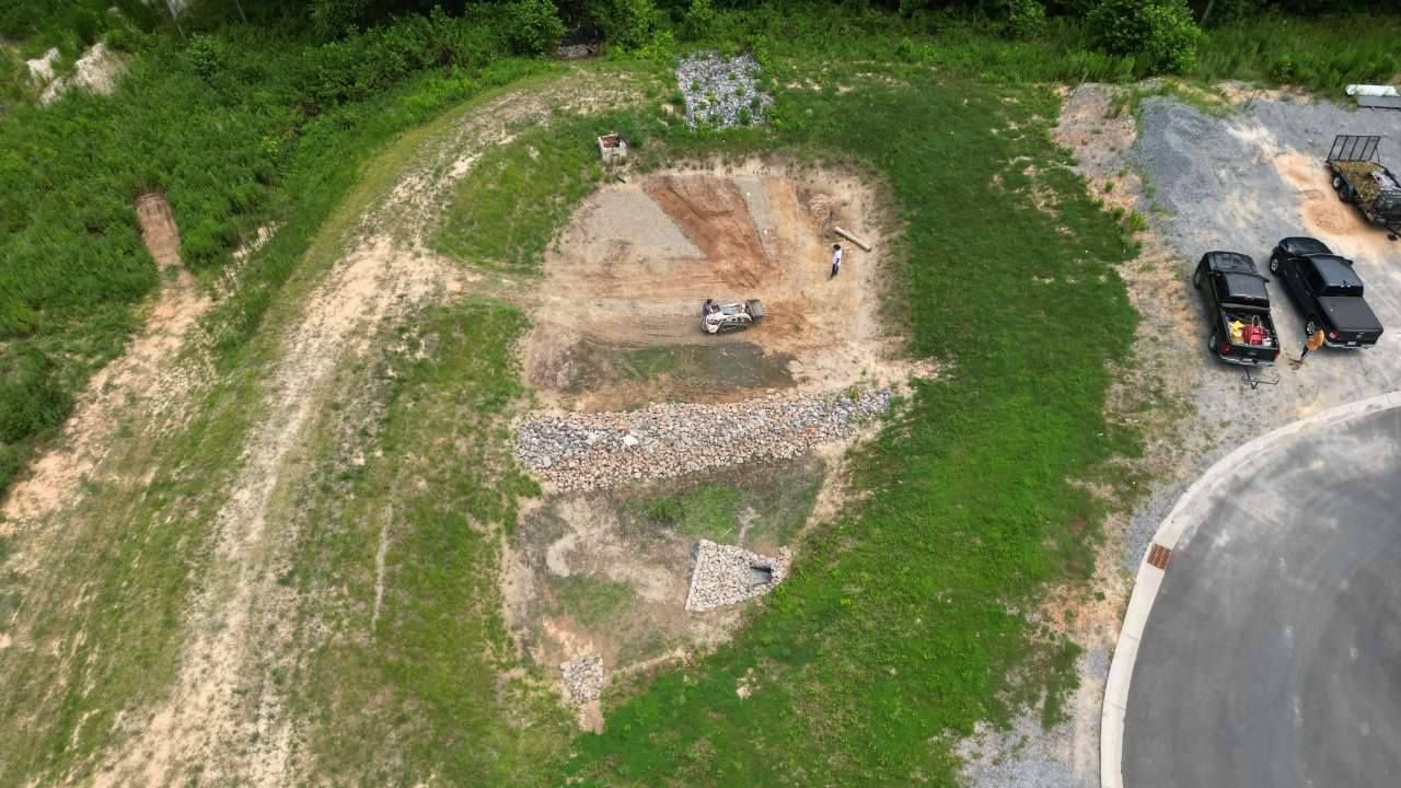 Aerial view of construction site with small excavator, dirt, rocks, and two trucks.