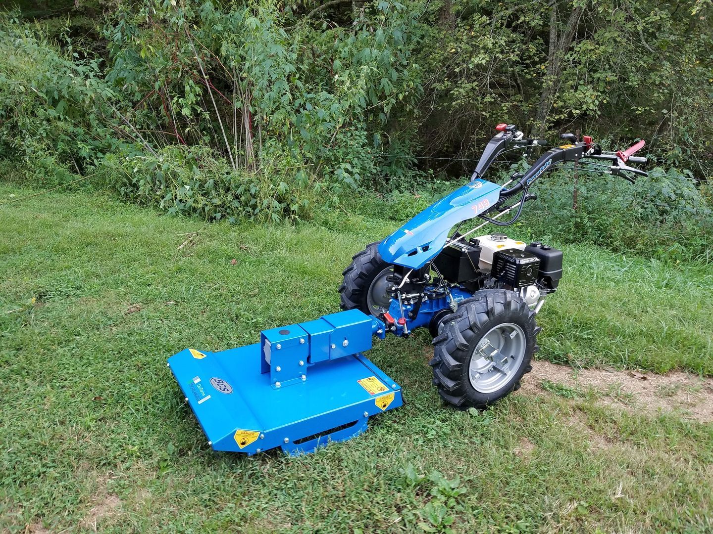 Yellow excavator digging in a grassy area near trees.