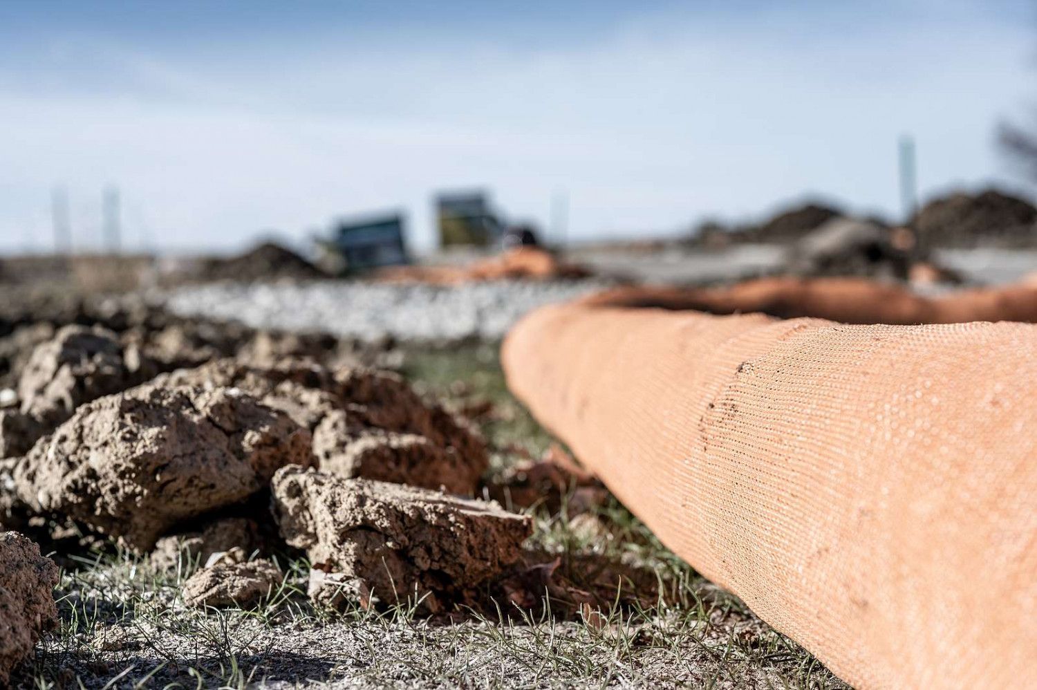 Orange pipe on the ground, construction site with dirt and equipment in the background.