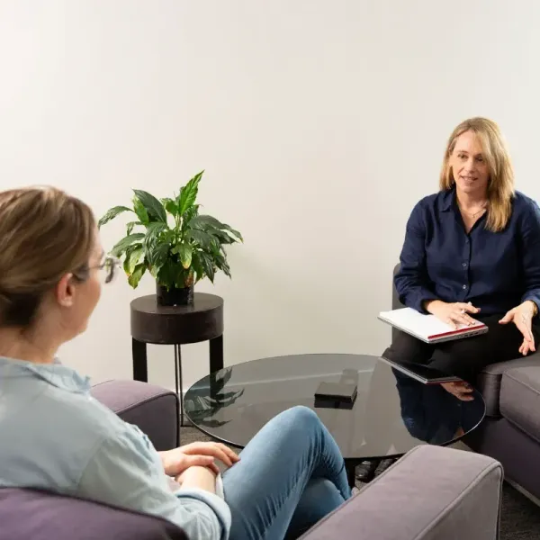 A woman is sitting on a couch talking to another woman during a occupational therapy assessment.