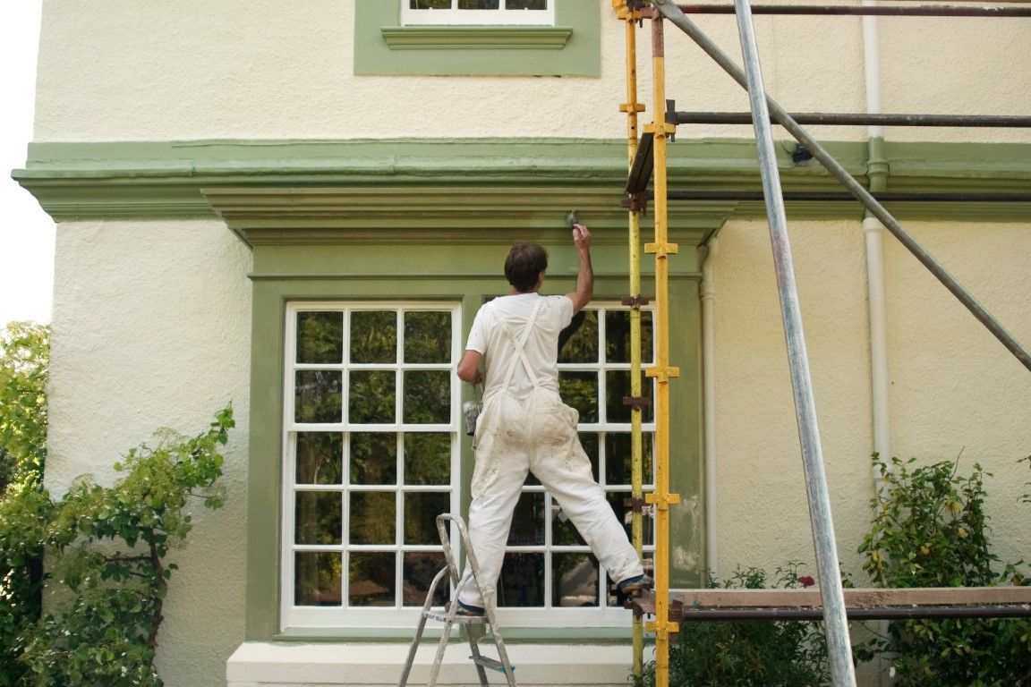 Man on a ladder painting the exterior of a house