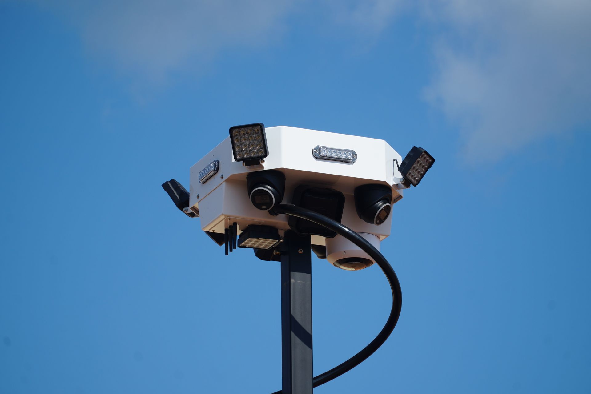 photorealistic mobile surveillance tower in a busy retail parking lot at sunset flashing blue lights visible modern security technology