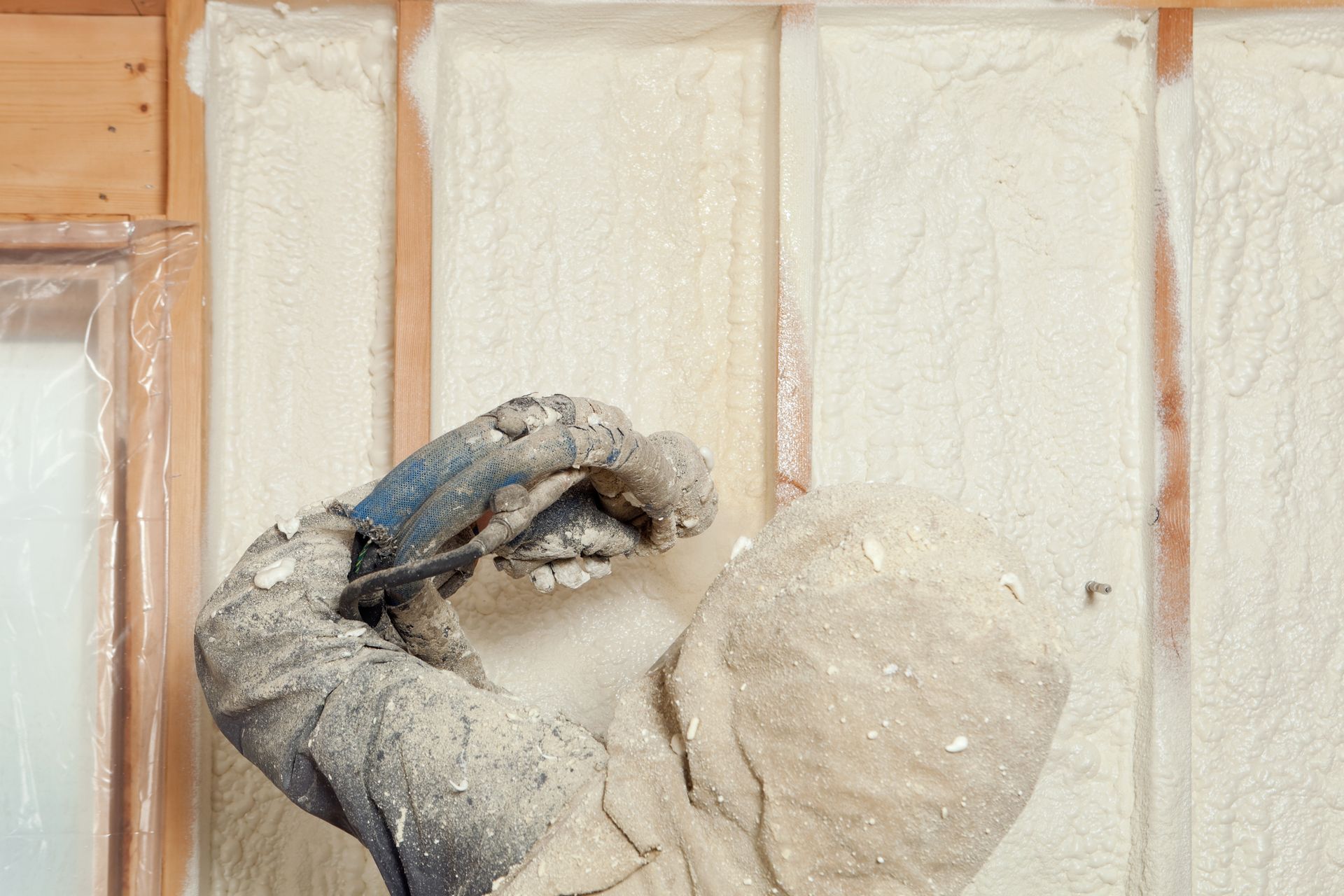 A man is spraying foam insulation on a wall.