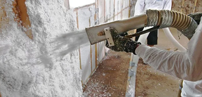 A person is blowing insulation into a wall with a machine.