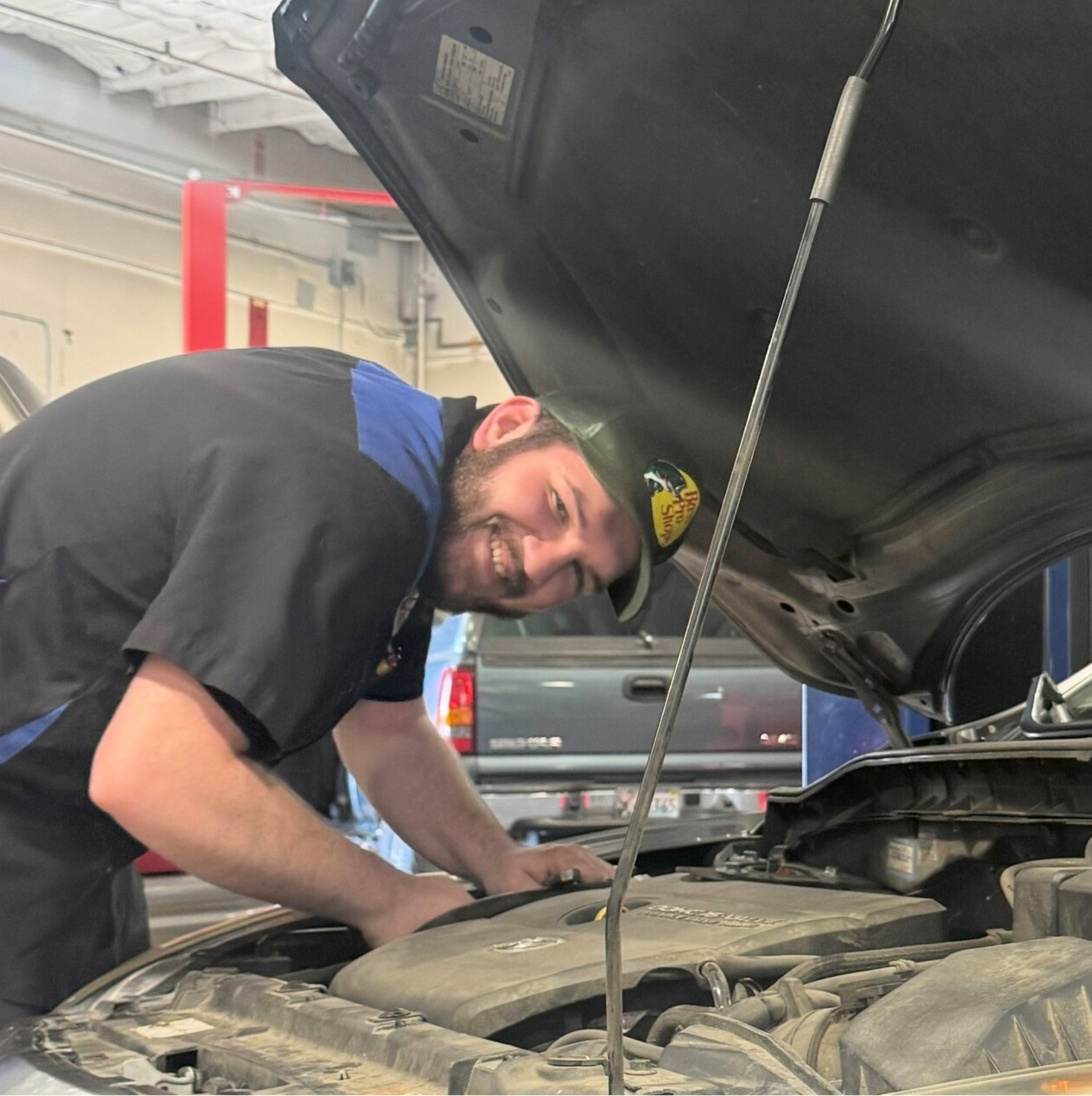 Austin Widmar - Mechanic smiling while working on a car engine in a garage. | Greg's Garage