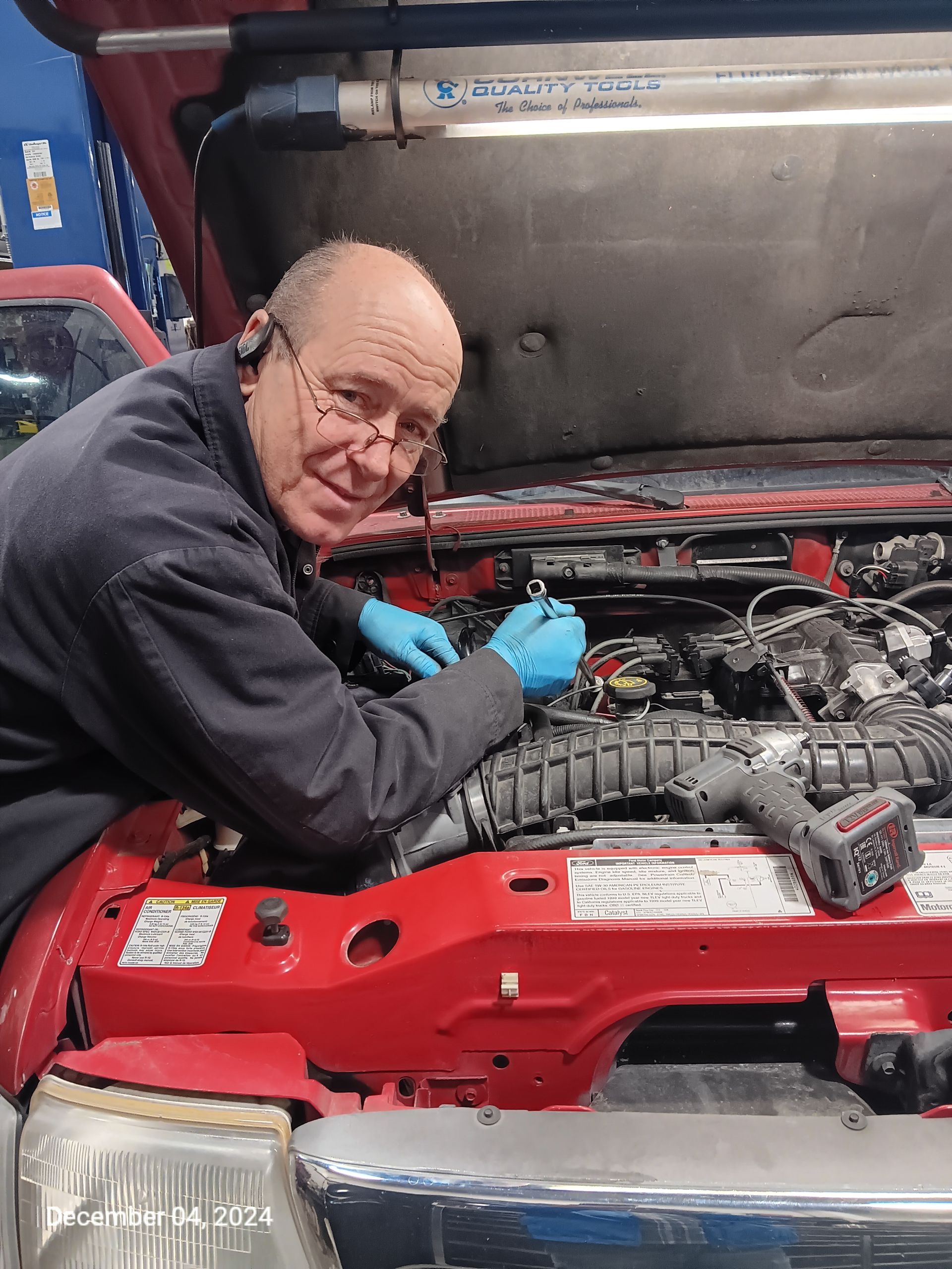 Curtis Roberts - Mechanic working on red truck engine, wearing gloves and glasses, smiles in garage. | Greg's Garage