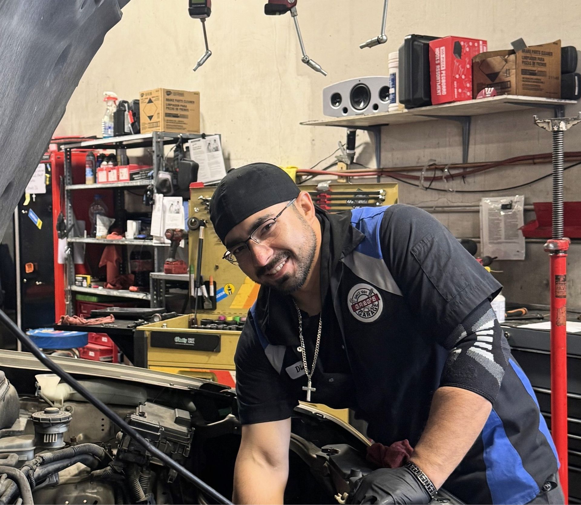 Diego Villa - Mechanic smiling, working on a car in a shop, wearing a cap and uniform. | Greg's Garage