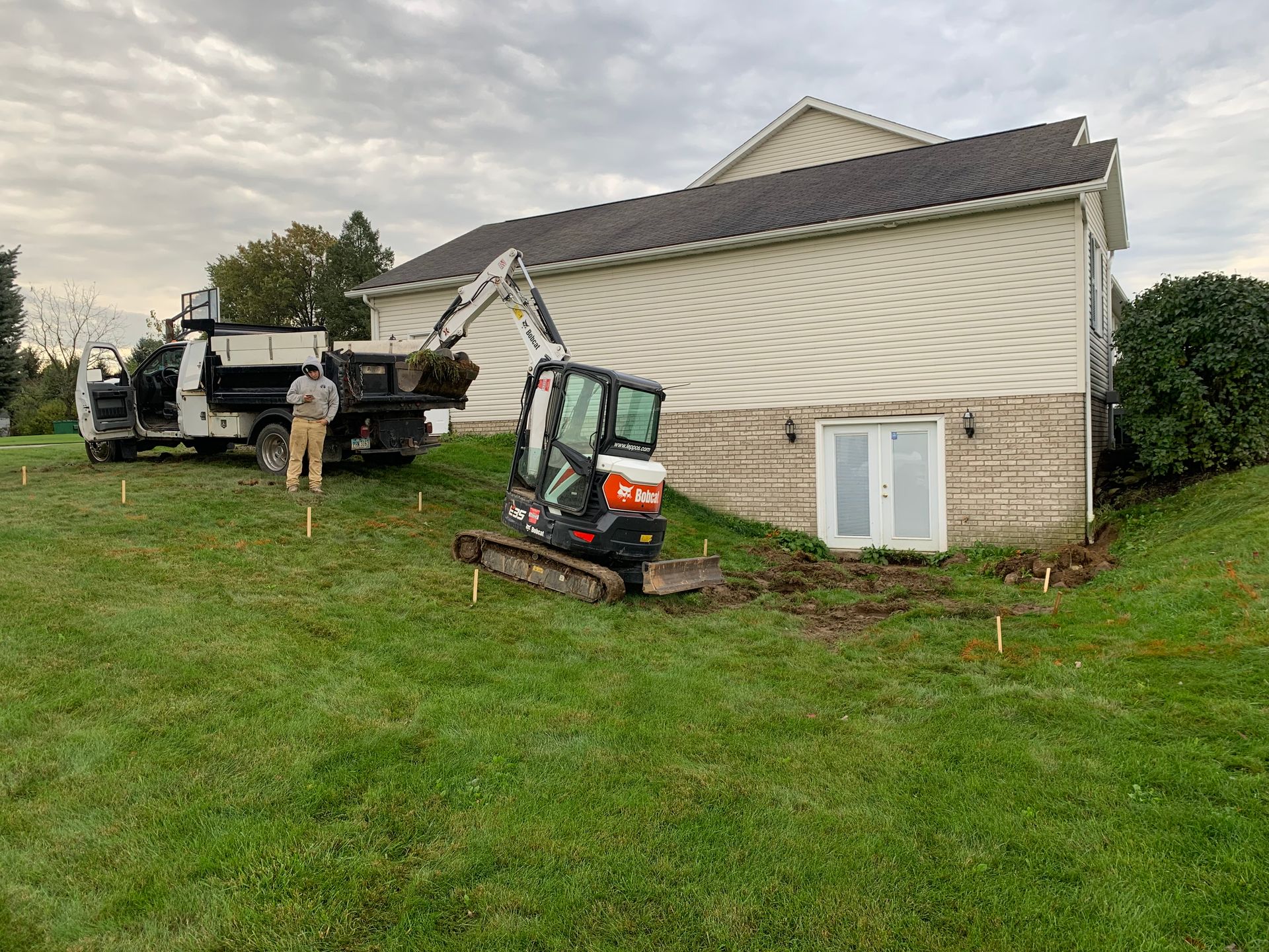 Construction site: Mini excavator and truck near a house, digging in the yard.