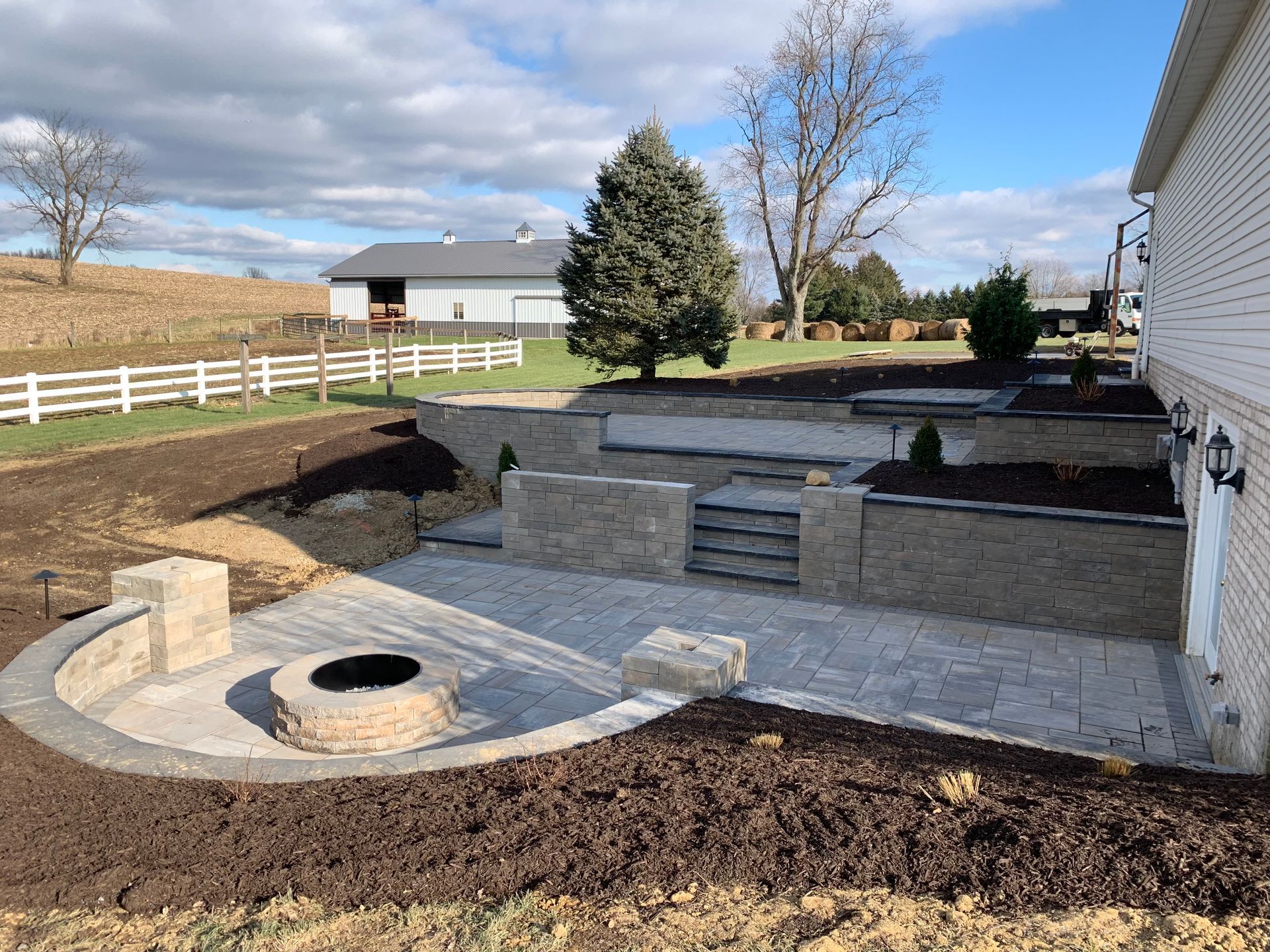 Backyard patio with fire pit, steps, and retaining walls; beige brick and grey pavers.