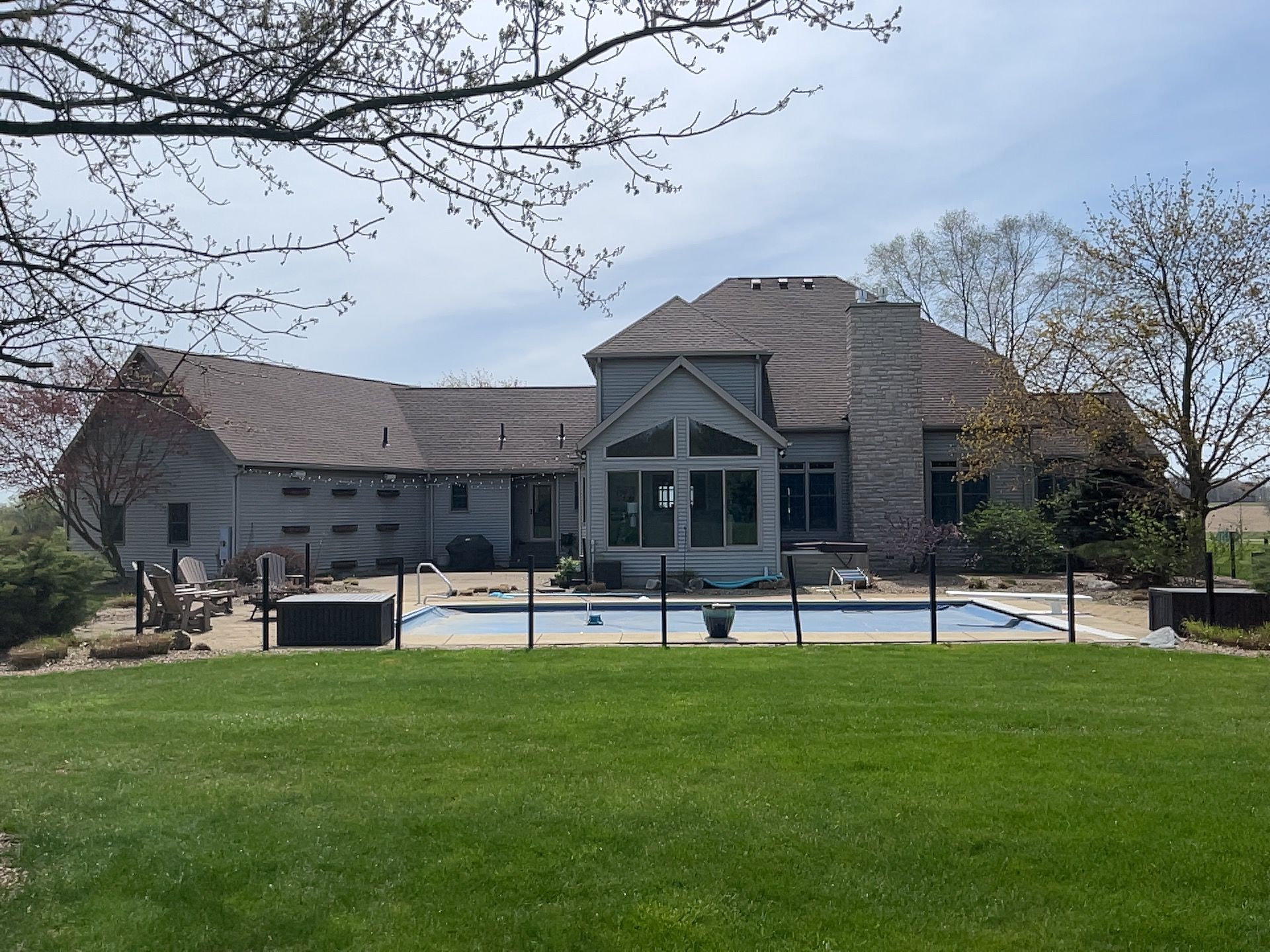 House with a swimming pool in backyard, gray siding, brown roof, and green lawn on a sunny day.