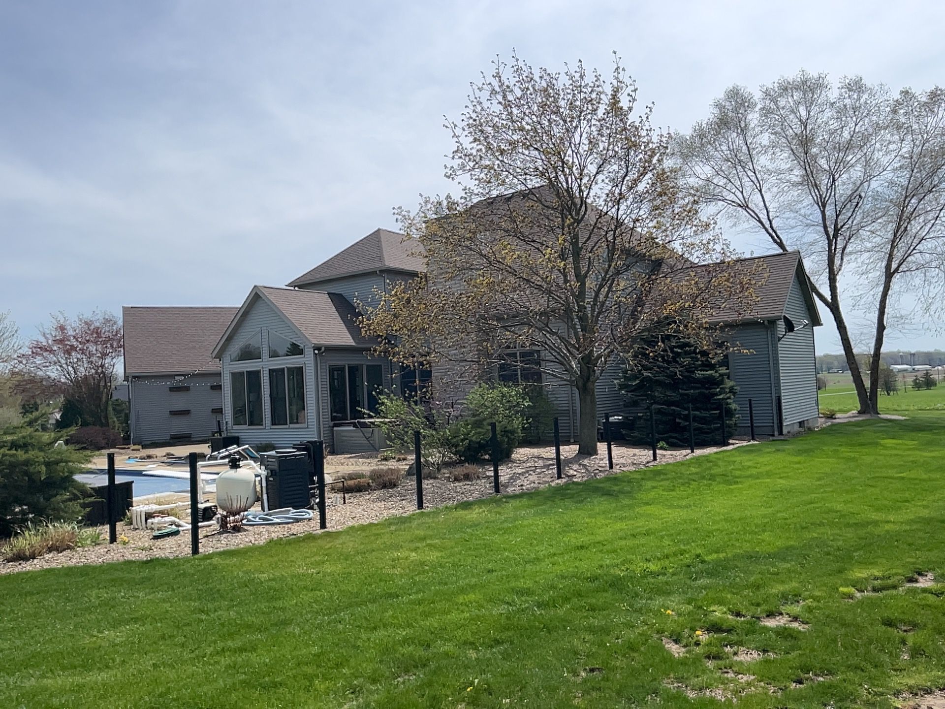 Large two-story house with a backyard pool, surrounded by a black fence and green grass on a sunny day.