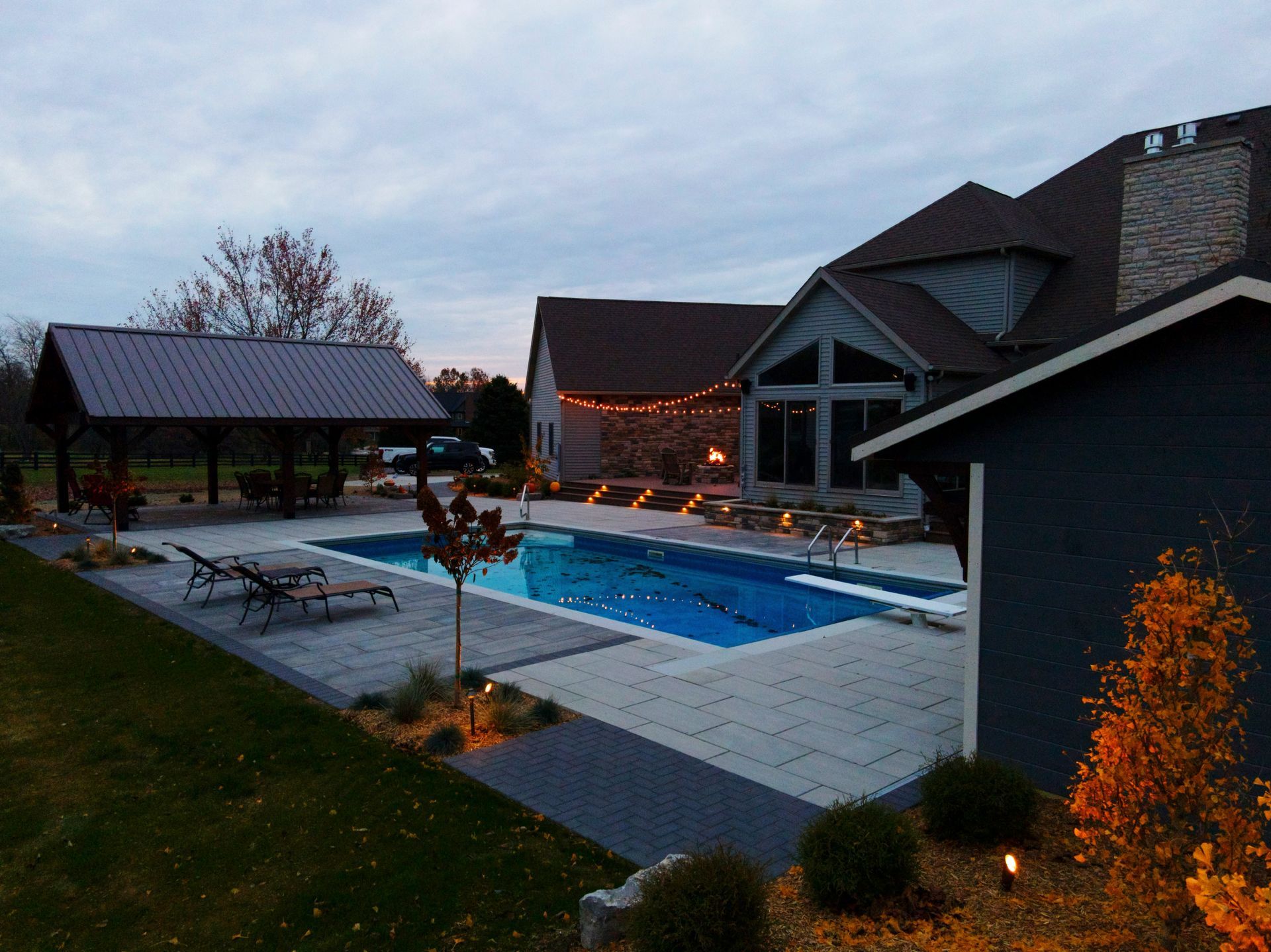 Backyard pool with a house and gazebo at dusk.