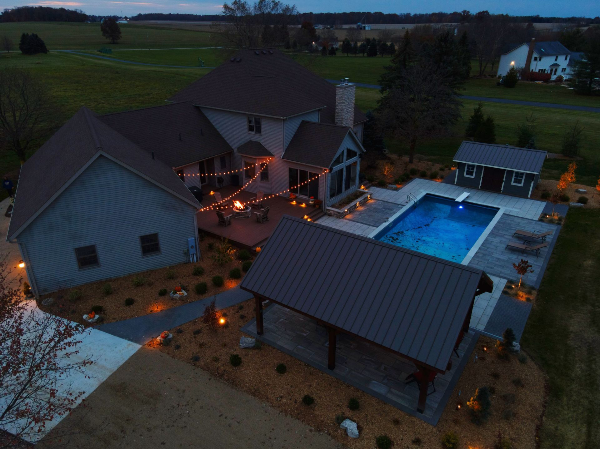 Aerial view of a home with a pool, patio, and outdoor lighting at dusk.