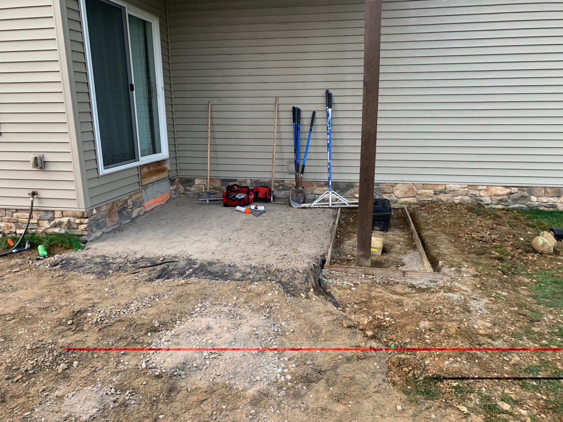 Concrete patio under construction next to a house with tools and gravel.