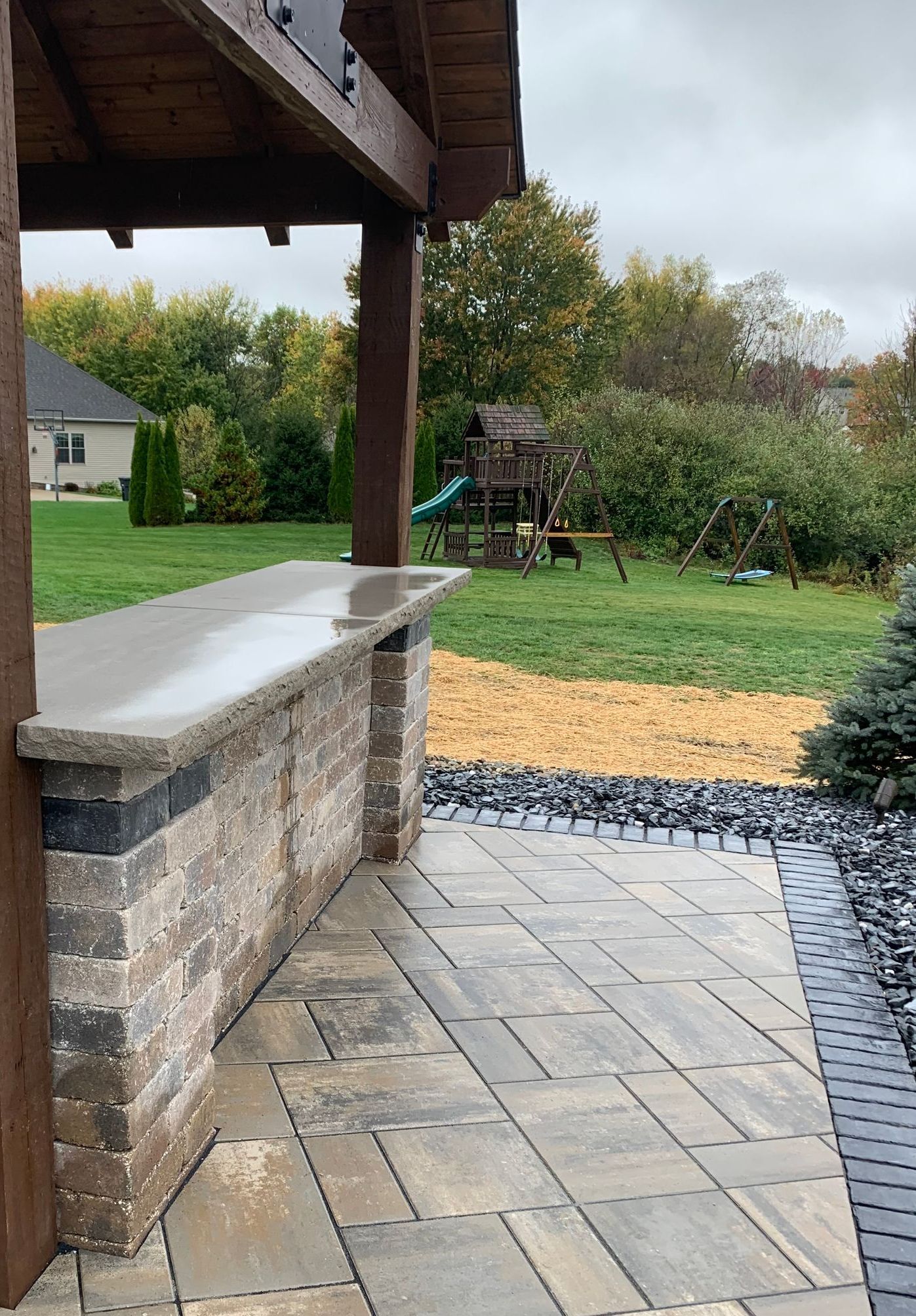 Outdoor bar with stone facade and concrete countertop. Backyard with playground in the distance.