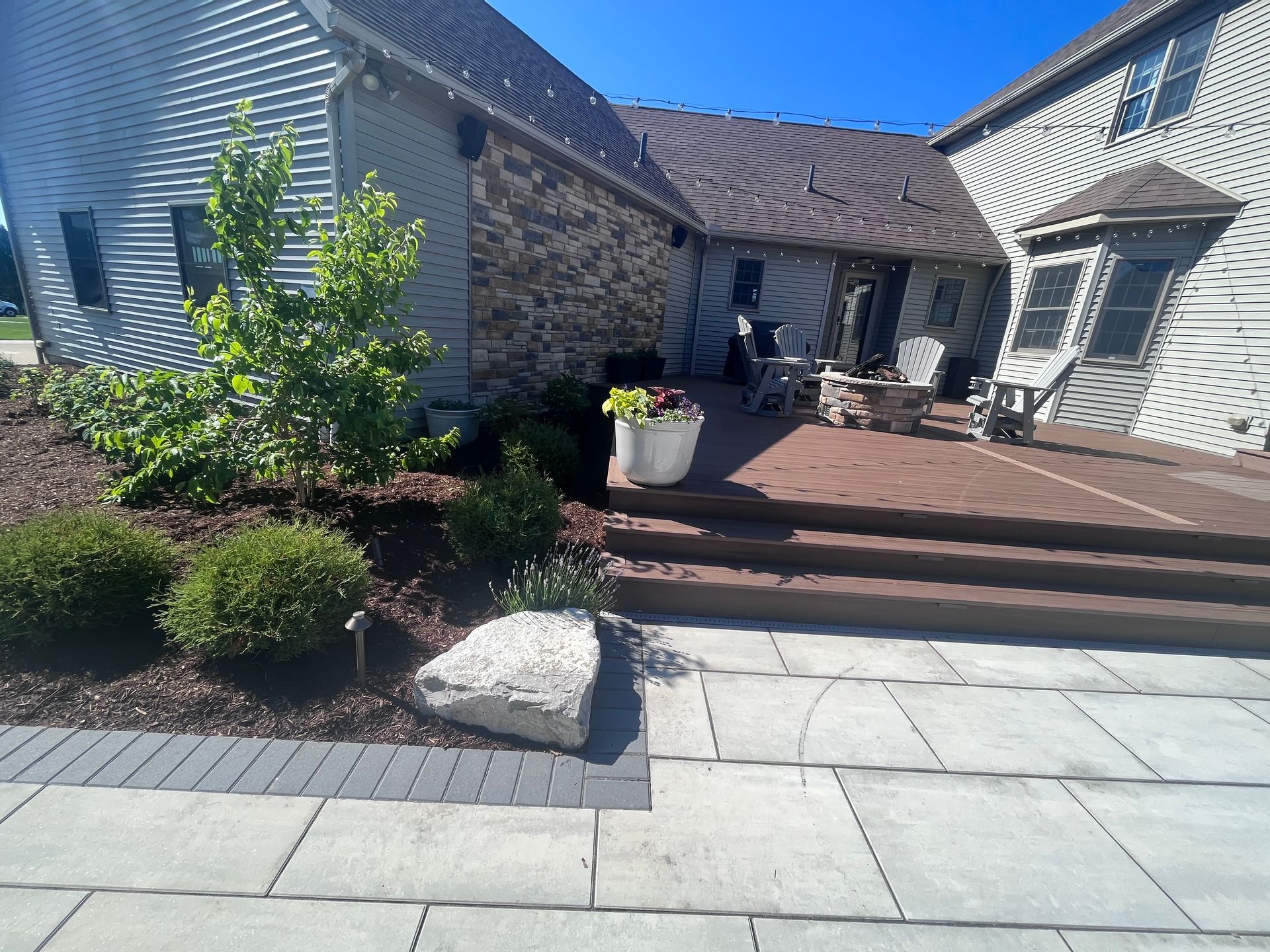 Backyard patio with stone walkway, wood deck, and landscaping.