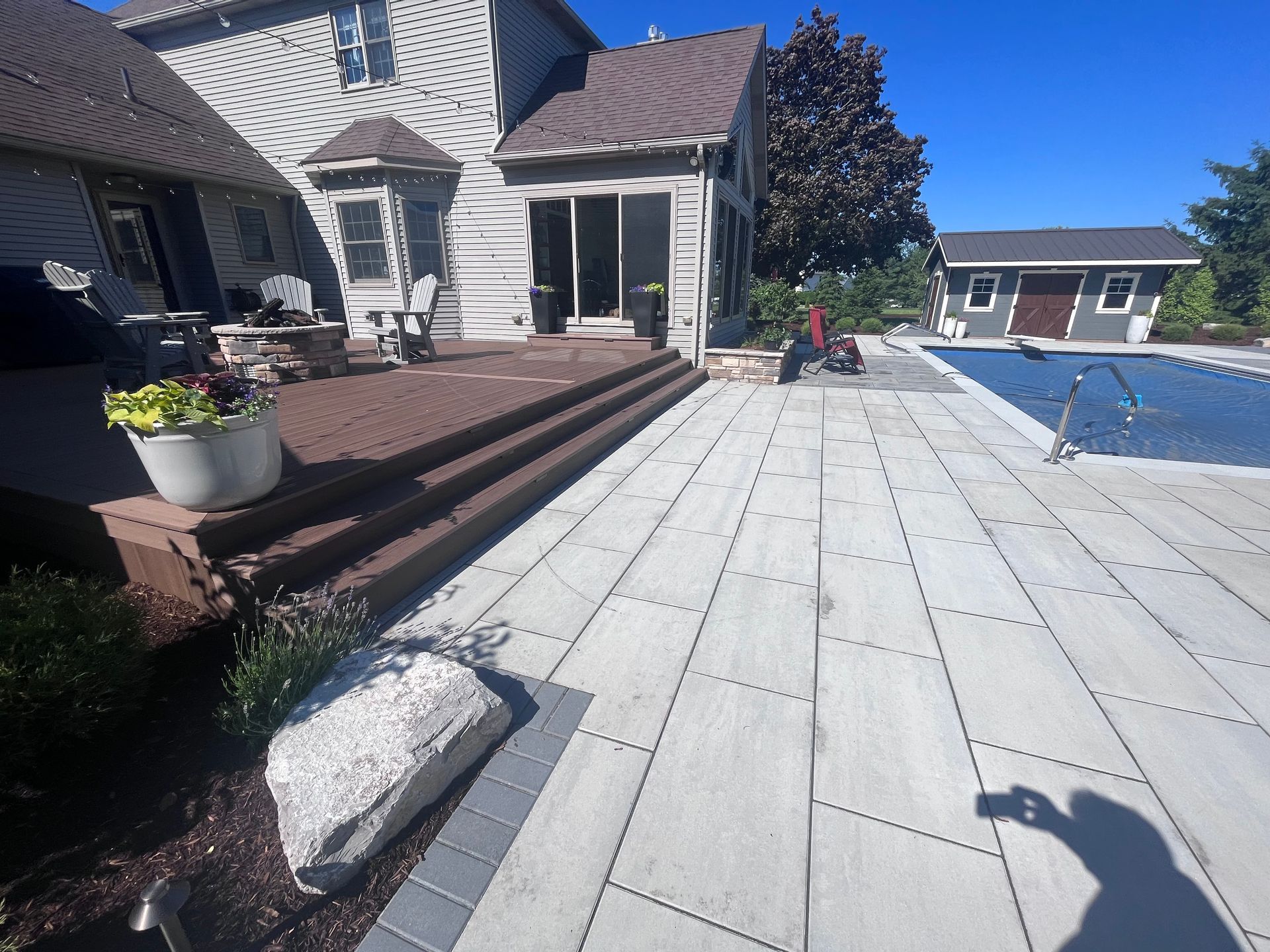 Backyard patio with steps leading to a house with sliding glass doors and a pool. Blue sky, sunny day.