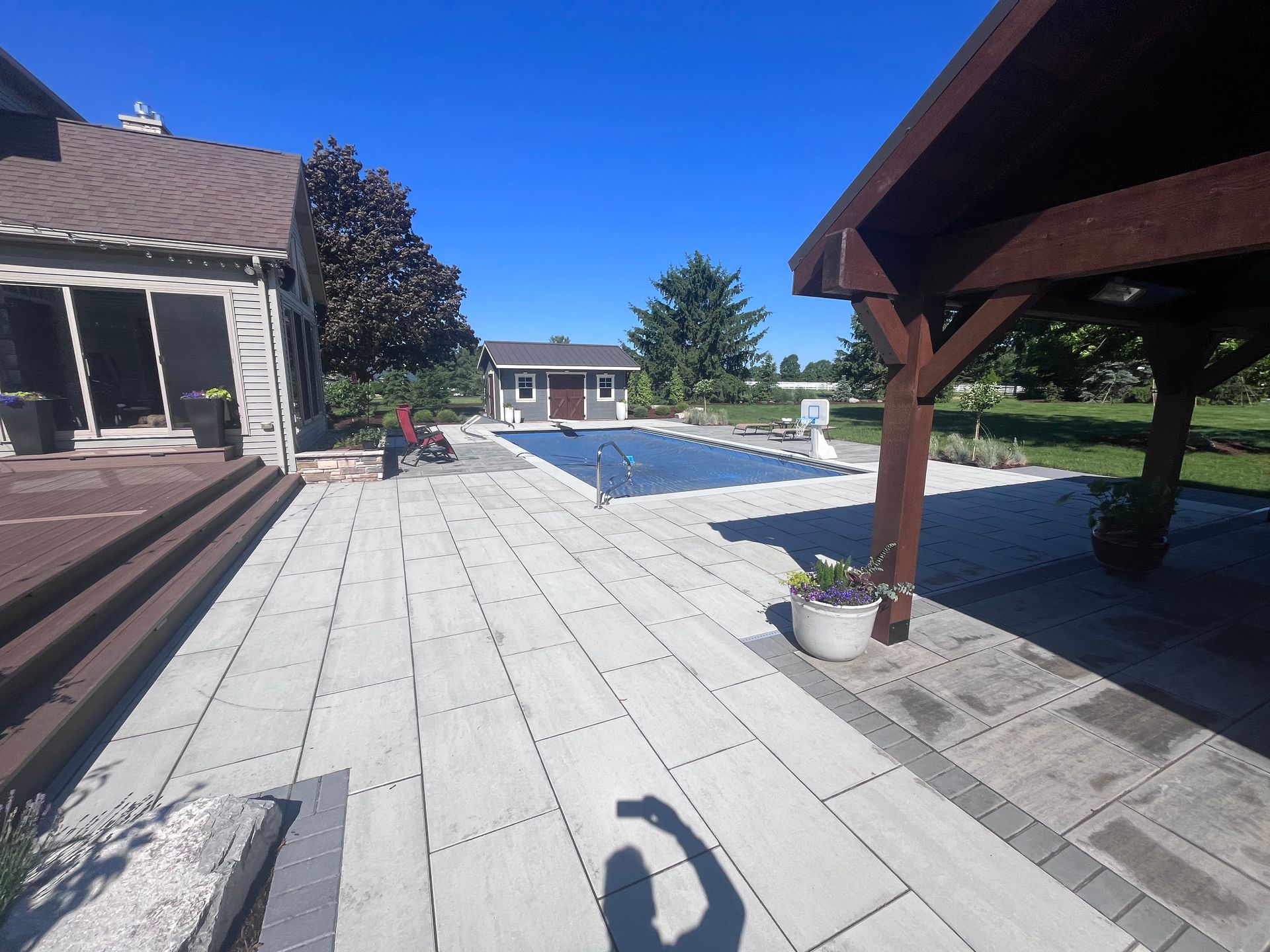 Patio with pool, covered with a blue tarp. Pergola on the right, house on the left. Sunny day.
