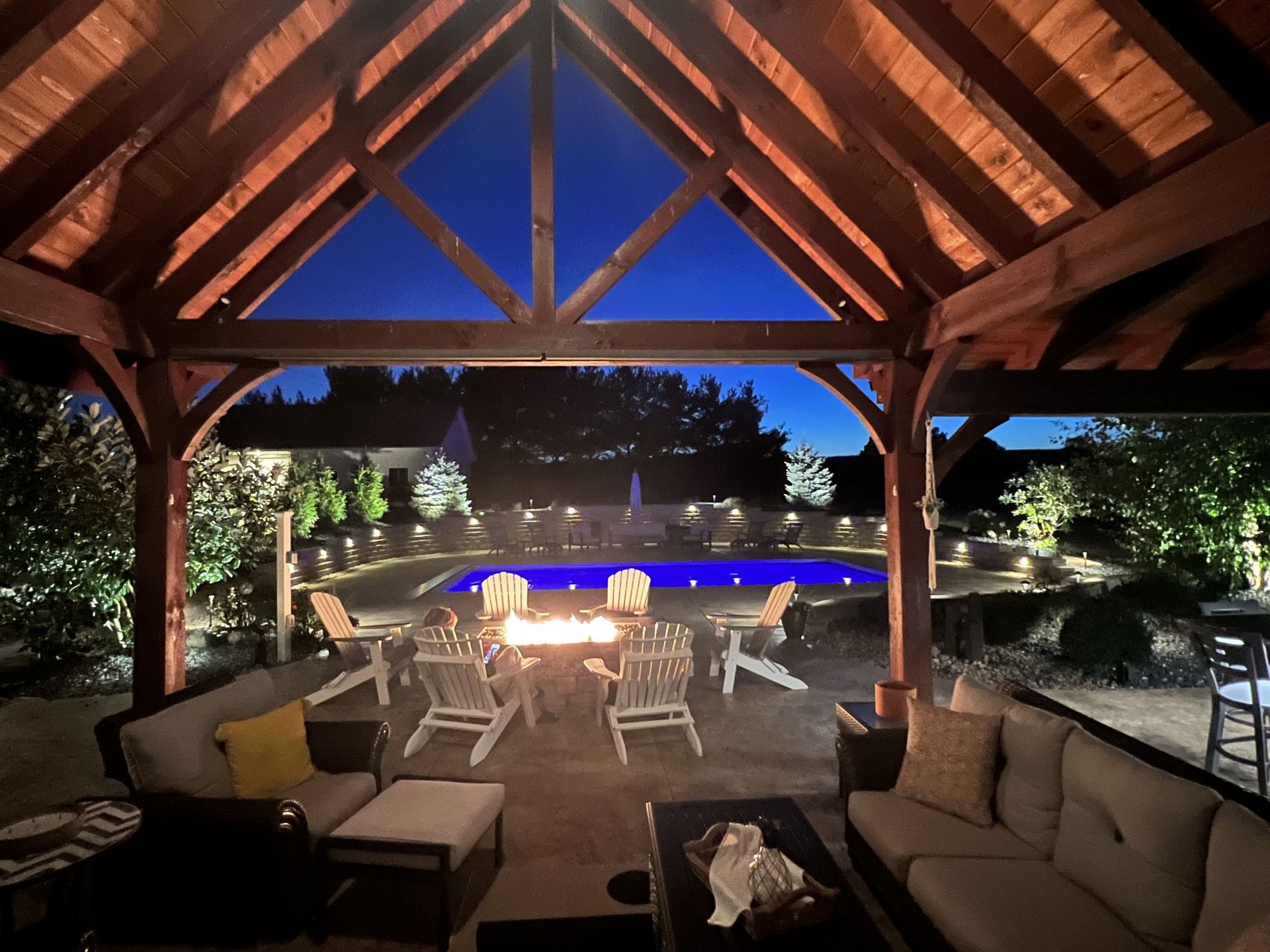Person's hands spread dark mulch around the base of a young tree in a grassy area, black pot in the background.