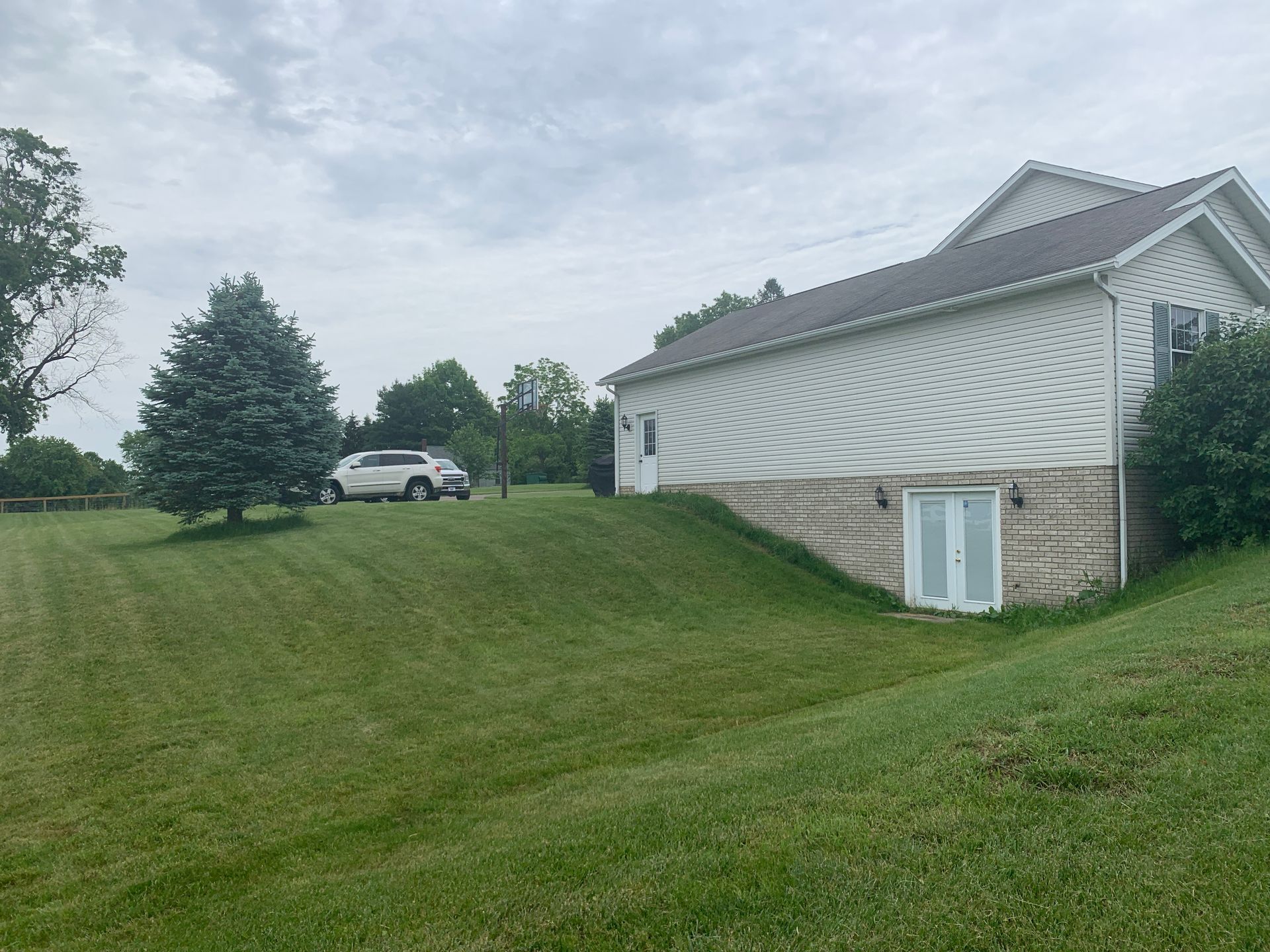 White house with a sloped lawn. A car is parked on the grass. Overcast sky.
