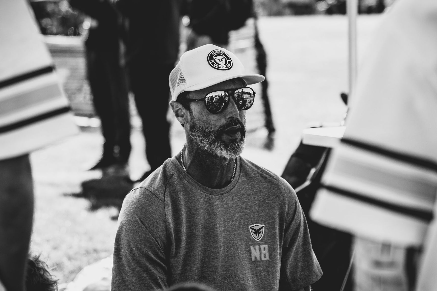 Ned Bowen coaching Fusion lacrosse with sunglasses and beard wearing a hat and shirt, outdoors.