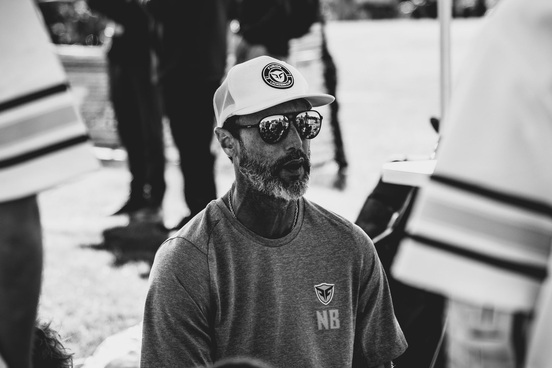 Ned Bowen coaching Fusion lacrosse with sunglasses and beard wearing a hat and shirt, outdoors.