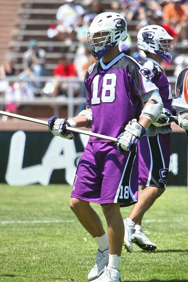 Ned Bowen lacrosse player for the MLL San Francisco Dragons in purple uniform, holding a stick, standing on a green field. Number 18 on jersey.