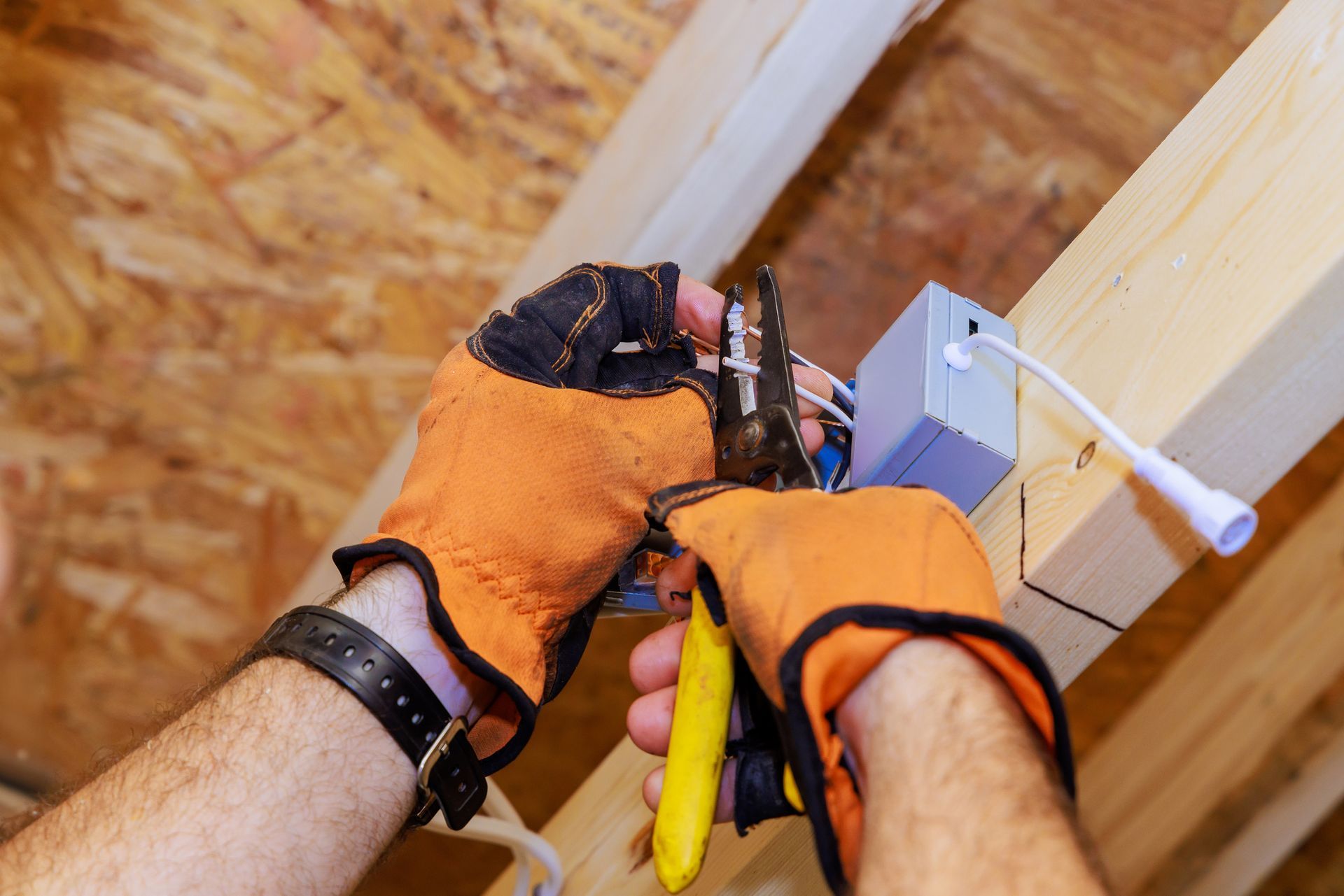 A man wearing orange gloves is working on an electrical box.