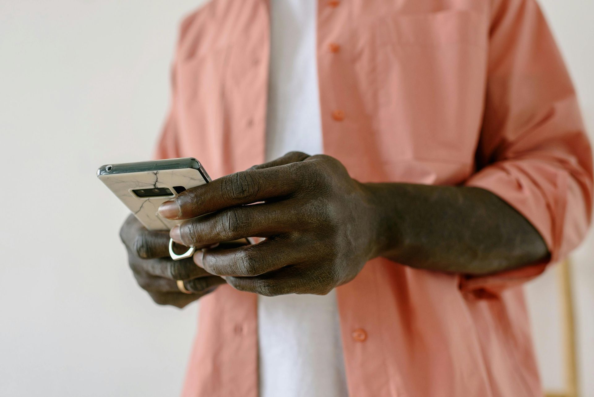A person wearing a peach-colored shirt holds a silver smartphone in their hands, focusing on the screen.