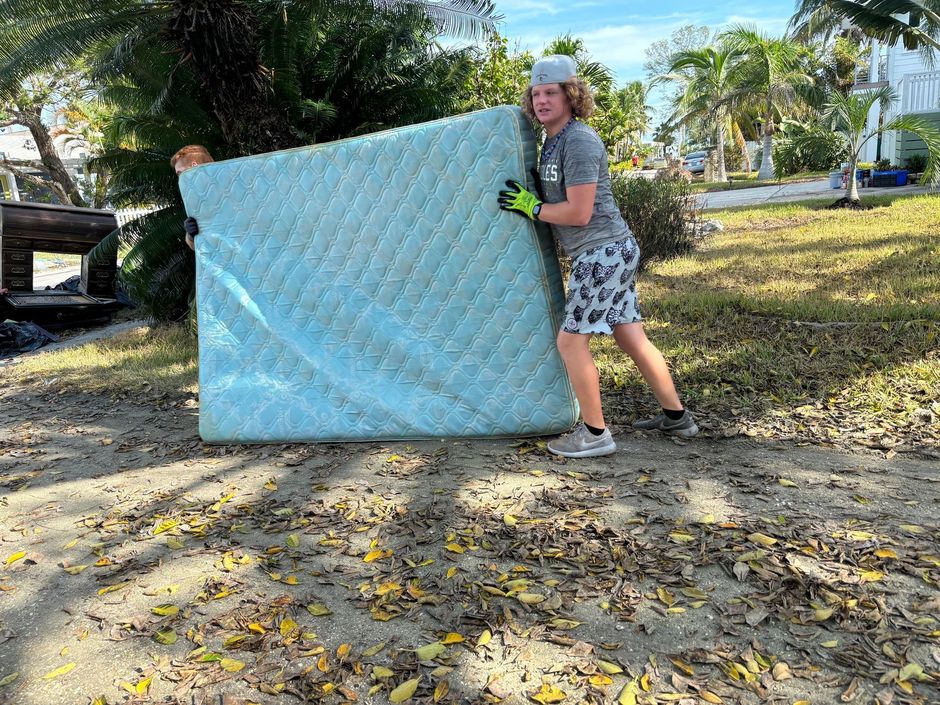 A man is carrying a large mattress in the dirt.