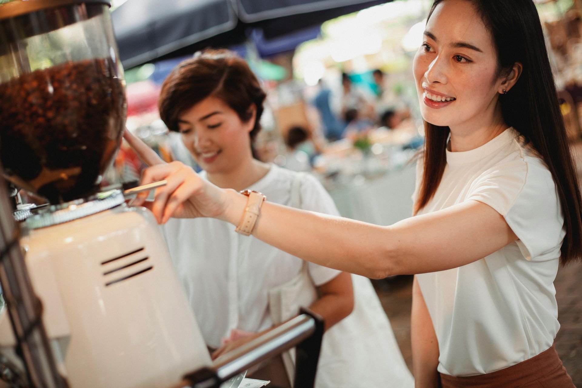 Two women are working on a coffee machine at a market.
