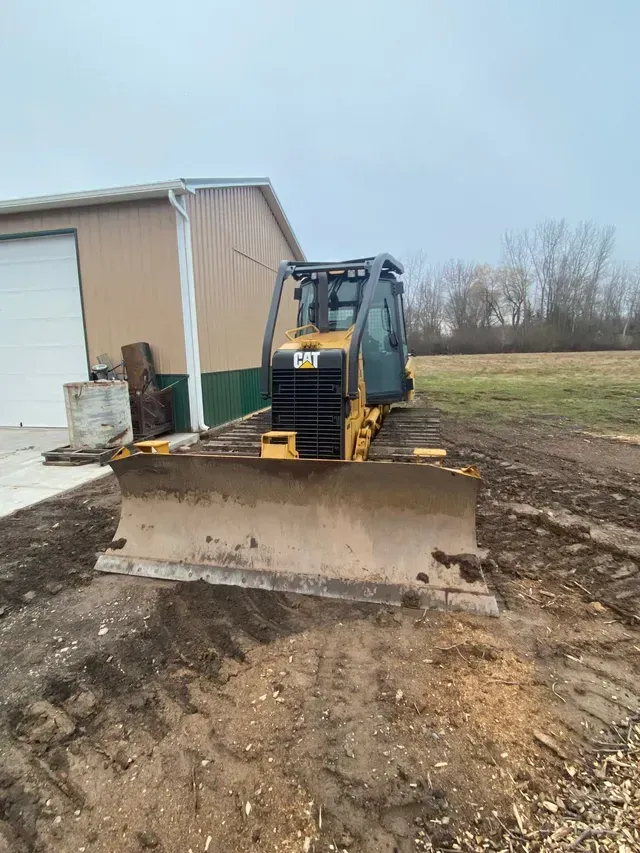 A bulldozer is parked in a dirt field in front of a building.
