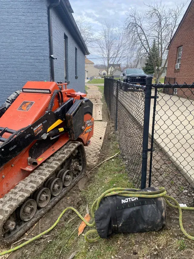 A small orange tractor is parked next to a chain link fence.