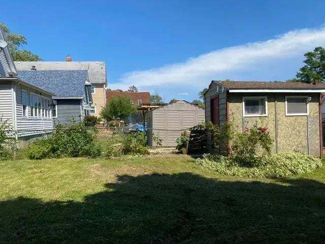 A backyard with a shed and a house in the background.