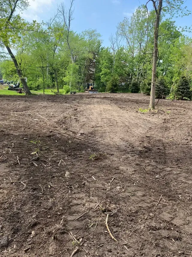 A dirt field with trees in the background and a house in the background.