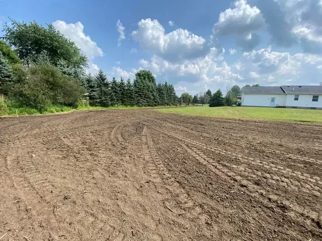 A large dirt field with a white house in the background