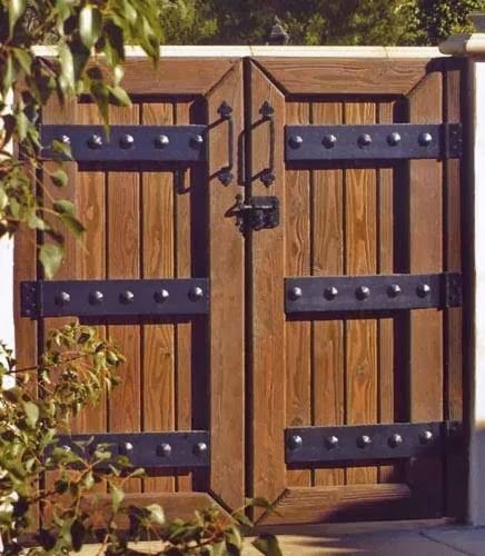 A wooden gate with black hinges is surrounded by trees