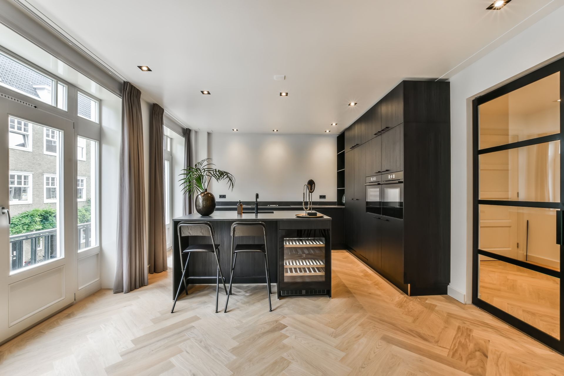 Cuisine moderne noire avec îlot central, cave à vin et parquet à chevrons.