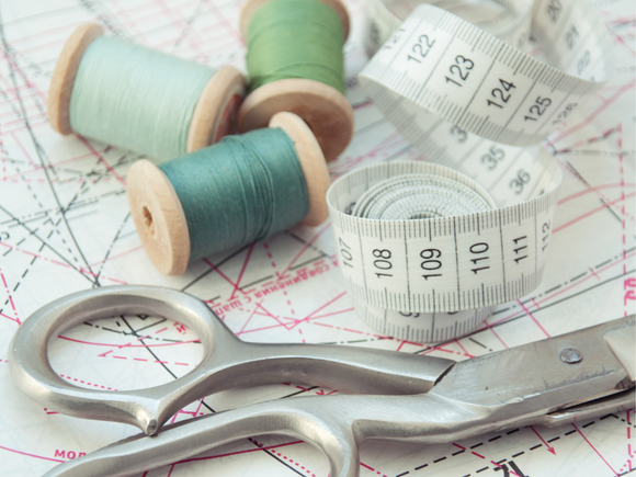 a sewing pattern, cotton reels, a measuring tape and scissors
