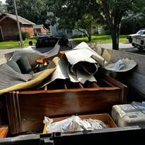 A truck bed filled with disassembled furniture, cushions, and debris in an outdoor setting.