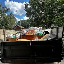 Truck bed filled with various trash, debris, and household items, likely for disposal.