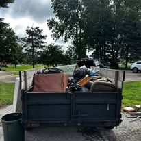 A dumpster filled with trash and various items, outdoors under a cloudy sky.