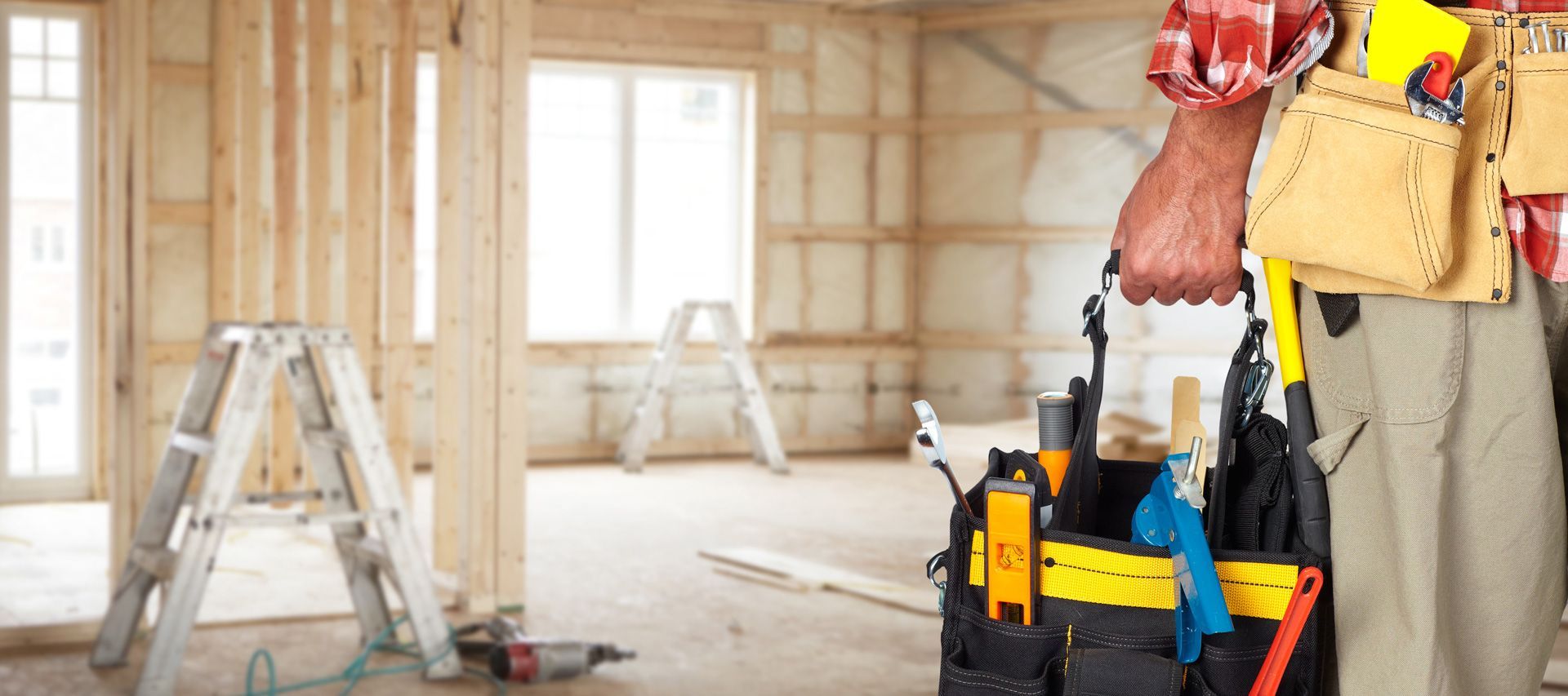 A man is holding a tool bag in a room under construction.