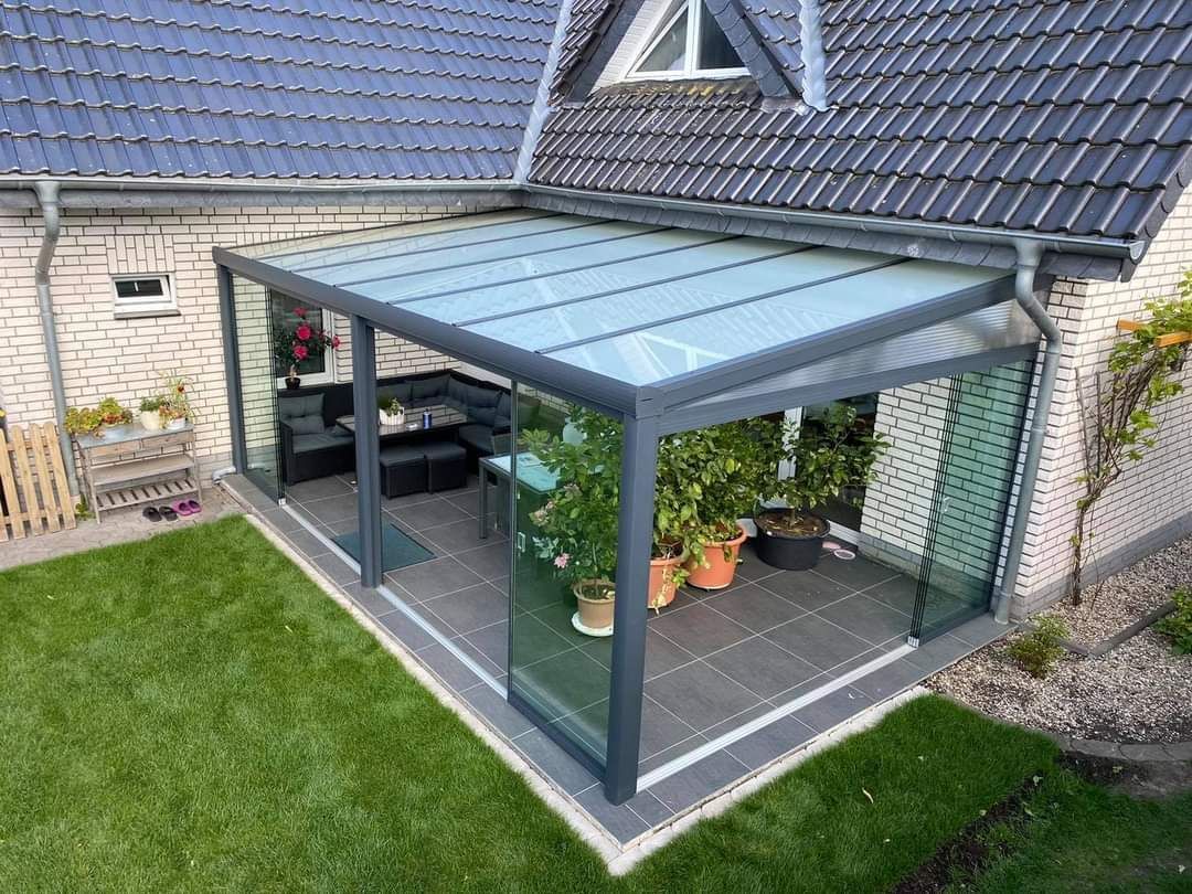 Een patio met glazen dak en glazen schuifdeuren voor een woning.