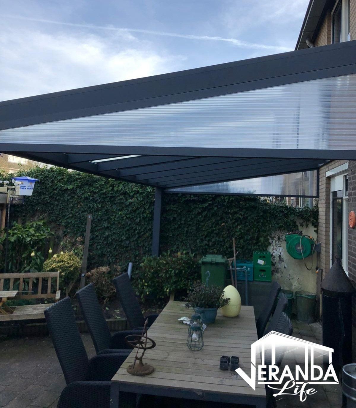 Een terras met een tafel en stoelen onder een baldakijn die veranda-leven zegt