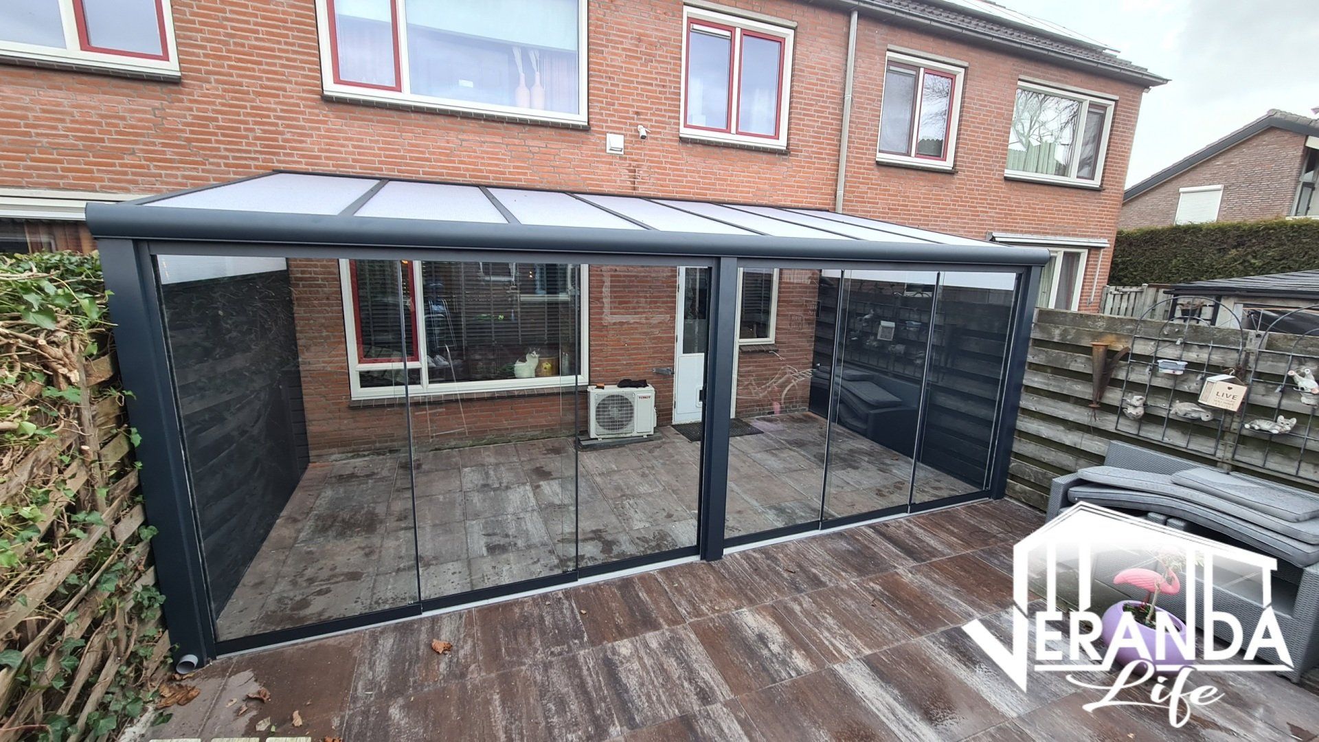 Een patio met overkapping en glazen schuifdeuren voor een bakstenen huis.