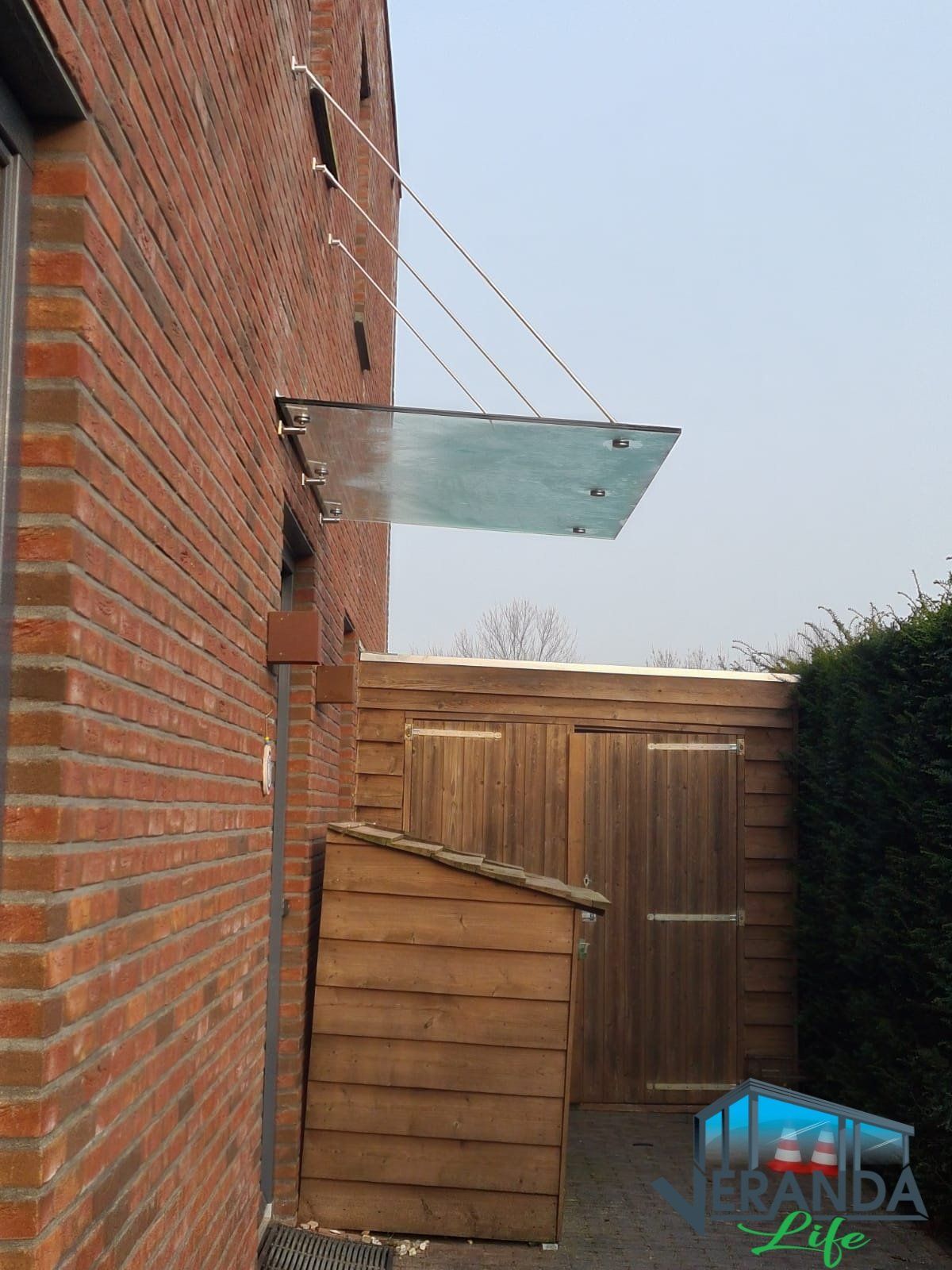 Aan de zijkant van een bakstenen gebouw is een glazen overkapping bevestigd.