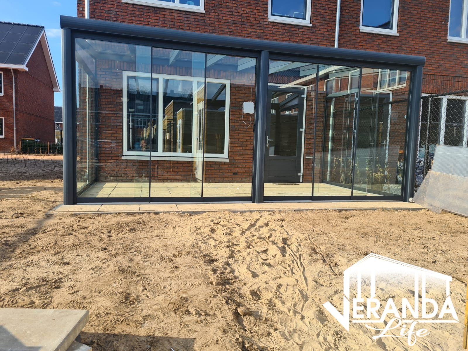 Voor een bakstenen huis wordt een grote glazen kamer gebouwd.